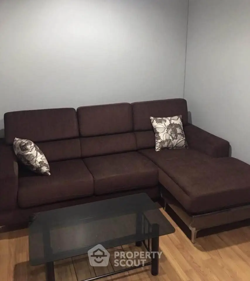 Modern living room with dark brown sectional sofa and glass coffee table on wooden floor.