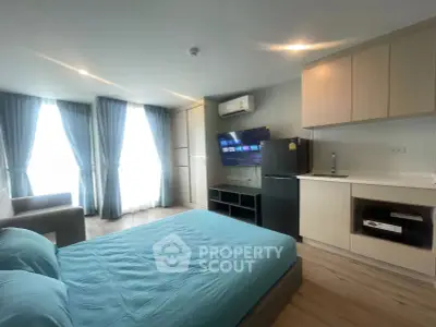 Modern studio apartment with open layout, featuring a cozy bed, kitchenette, and natural light from large windows.