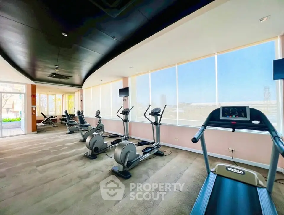 Spacious gym with modern exercise equipment and large windows offering natural light.