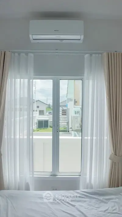 Bright bedroom with large window and air conditioning, offering a serene view.