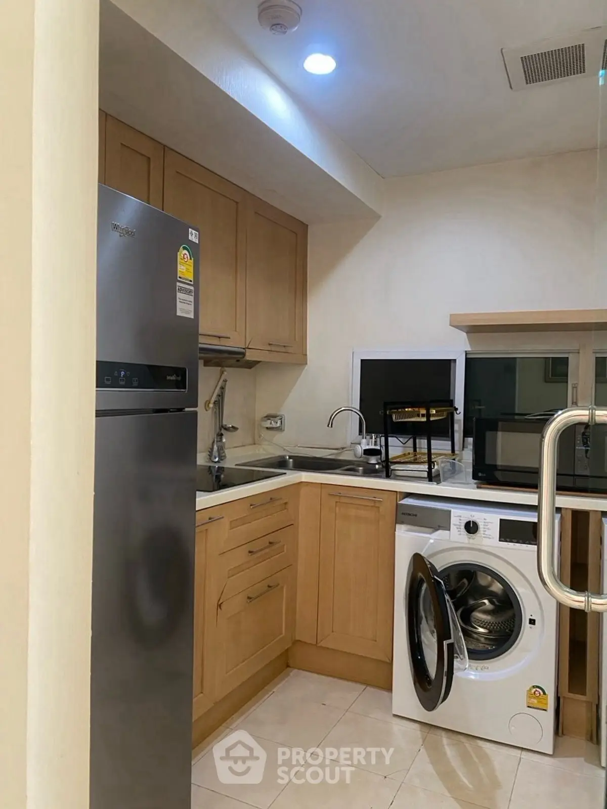 Modern kitchen with wooden cabinets, stainless steel fridge, and washing machine in cozy apartment.