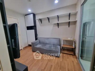 Modern living room with sleek sofa and open shelving, adjacent to a glass door leading to the kitchen.