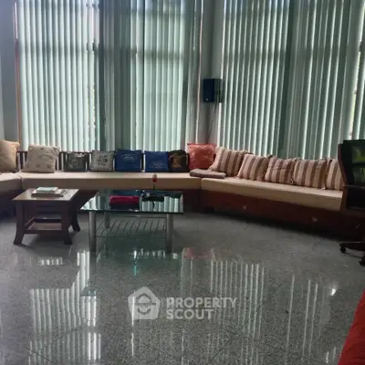 Spacious living room with elegant seating and large windows with vertical blinds.