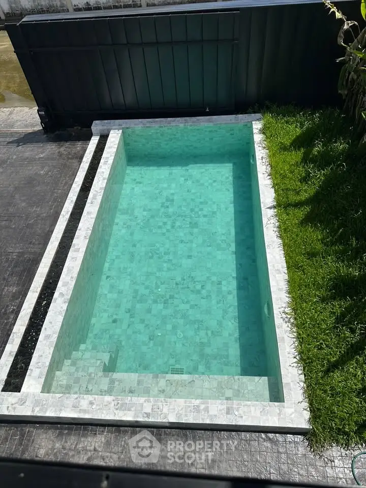 Modern rectangular swimming pool with elegant tile design and lush green surroundings.