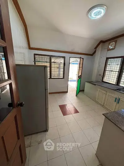 Spacious kitchen with tiled floor and ample natural light, featuring a large refrigerator and open layout.