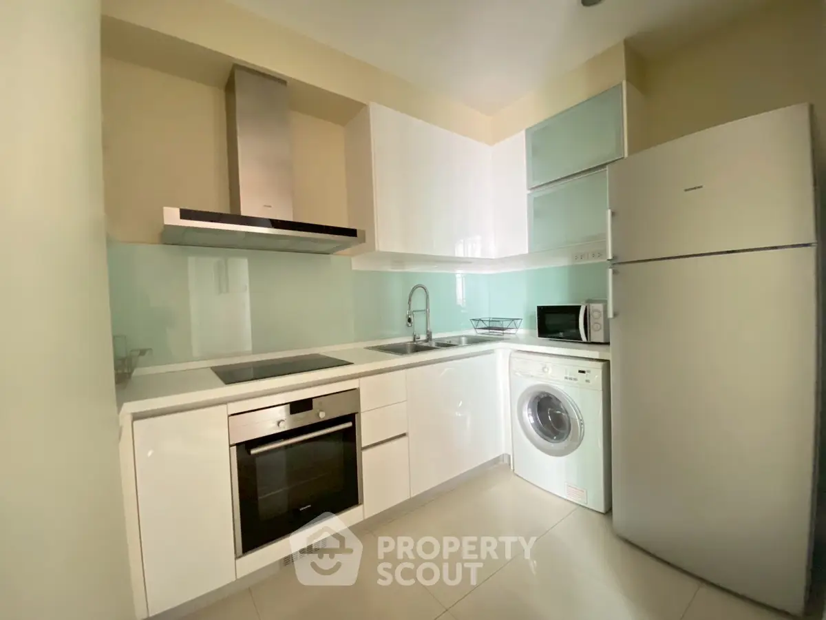 Modern kitchen with sleek appliances and white cabinetry, featuring a washing machine and oven.