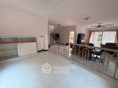 Spacious open-plan living room with elegant staircase and large windows for natural light.