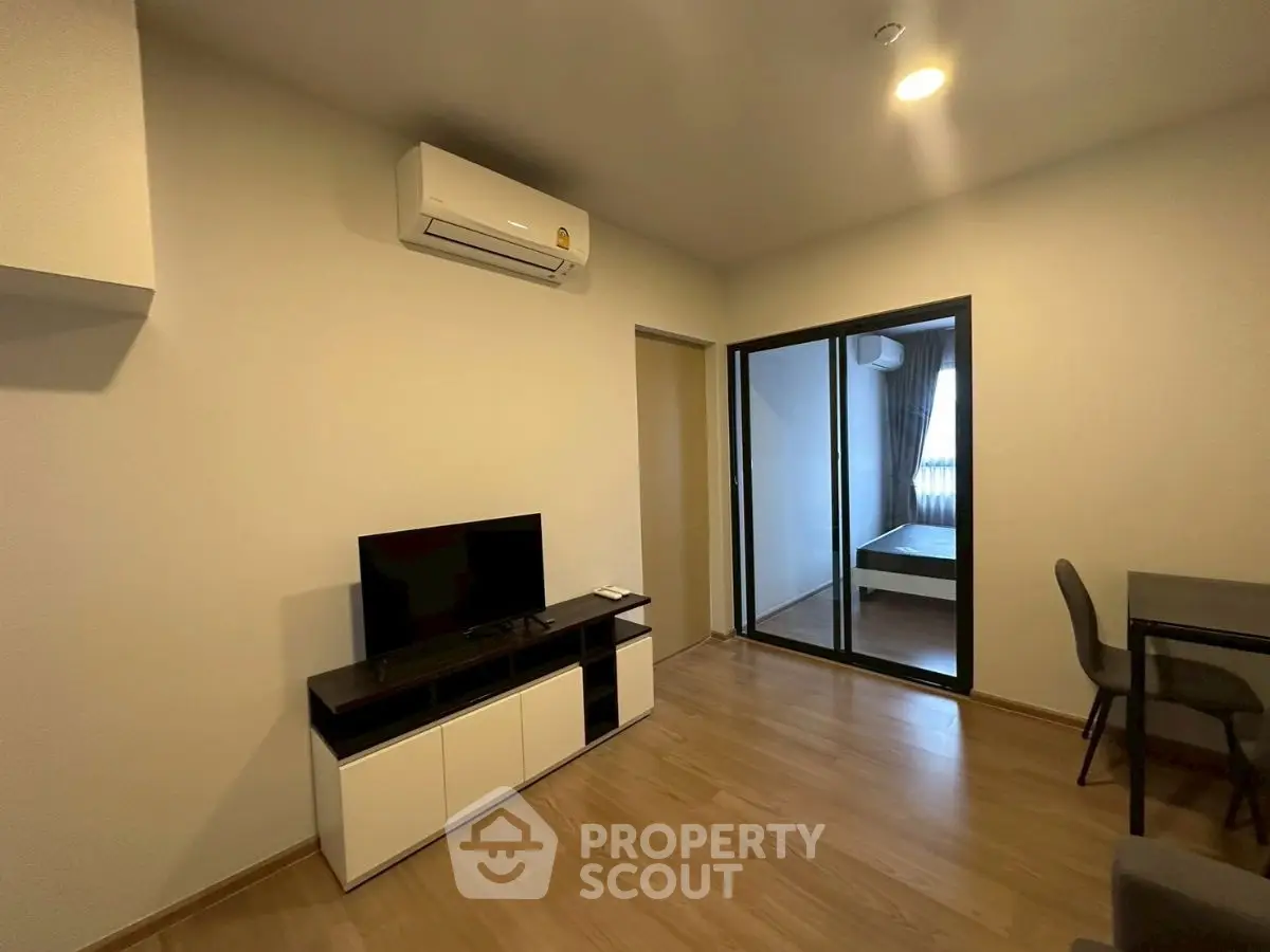 Modern living room with sleek furniture and wooden flooring, featuring a TV and air conditioning unit.