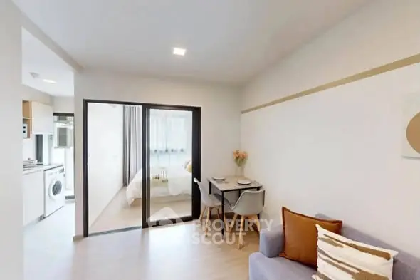 Modern open-plan living room with dining area and view into bedroom, featuring sleek decor.
