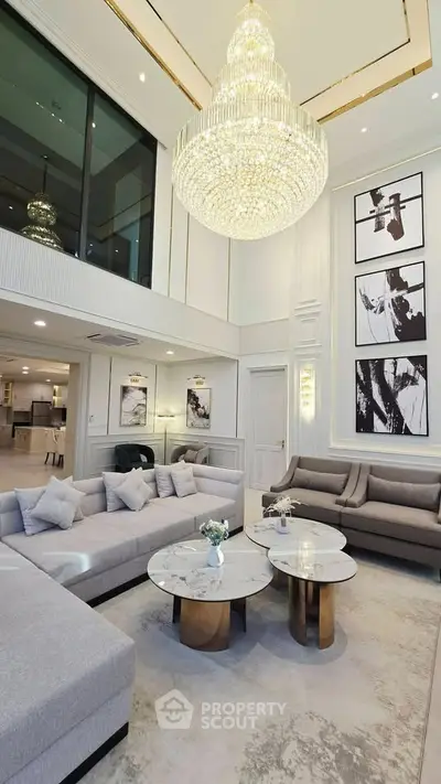 Luxurious living room with high ceiling, elegant chandelier, and modern decor in a spacious open layout.