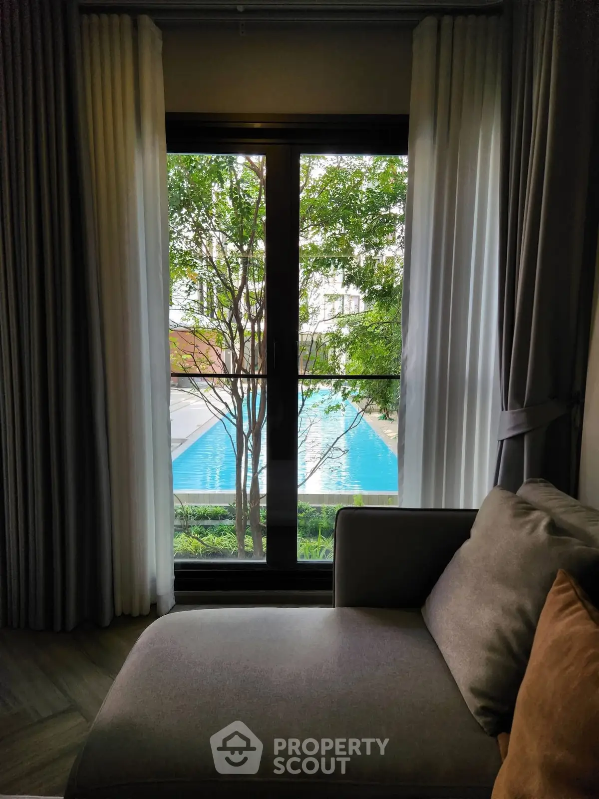 Cozy living room with pool view through large window, elegant curtains and comfortable sofa.