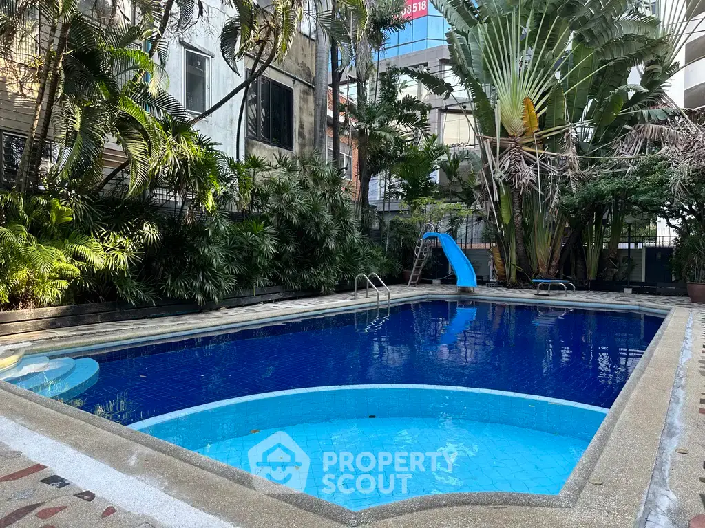 Stunning outdoor pool area with lush greenery and slide, perfect for relaxation and leisure in urban setting.