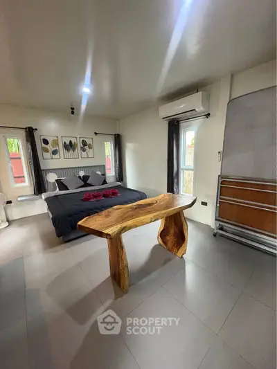 Spacious bedroom with modern decor and unique wooden table, featuring large windows and stylish artwork.