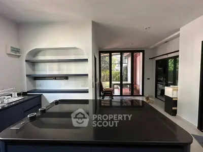 Modern kitchen with sleek black countertops and open layout, leading to a bright living area with garden view.