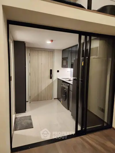 Modern compact kitchen with sleek appliances and sliding glass doors in a stylish apartment.