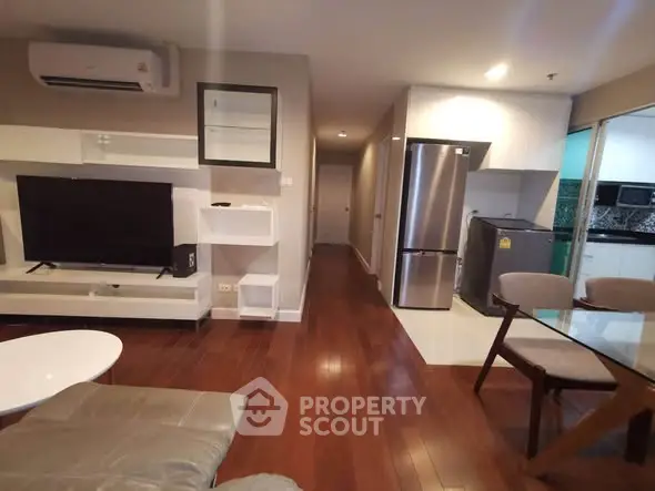 Modern living room with wooden flooring, sleek furniture, and integrated kitchen appliances.