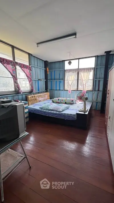 Cozy bedroom with wooden flooring and large windows offering natural light.