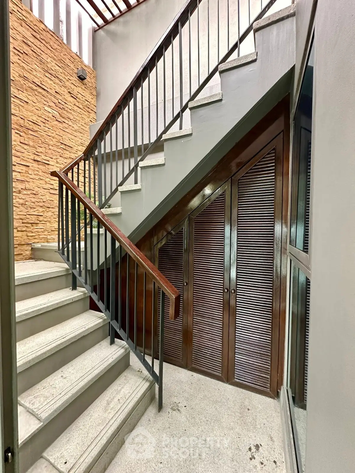 Stylish modern staircase with wooden accents and stone wall in a contemporary home.