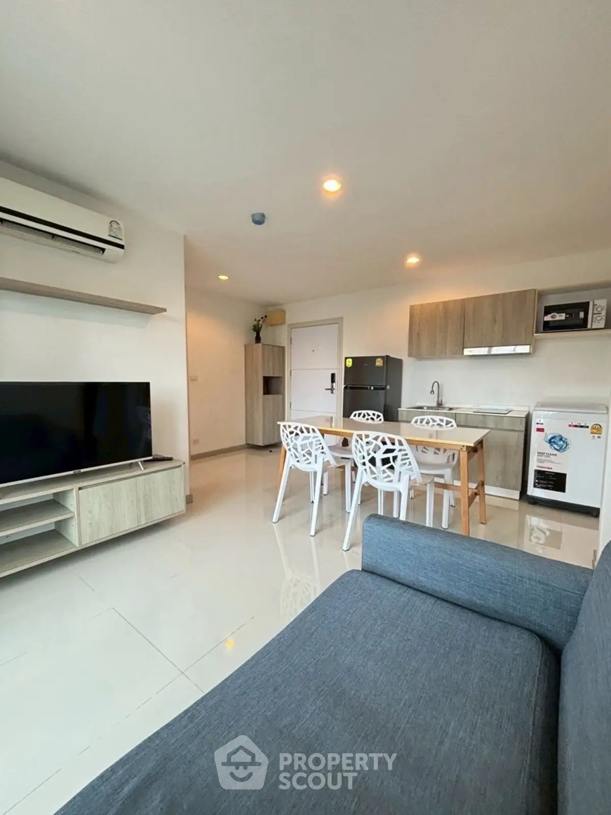 Modern open-plan living room with kitchen and dining area, featuring sleek furniture and appliances.