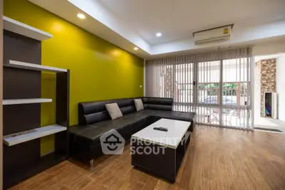 Modern living room with sleek black sofa, wooden flooring, and vibrant green accent wall.