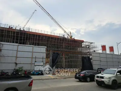 Construction site of a modern building with cranes and scaffolding under a cloudy sky.