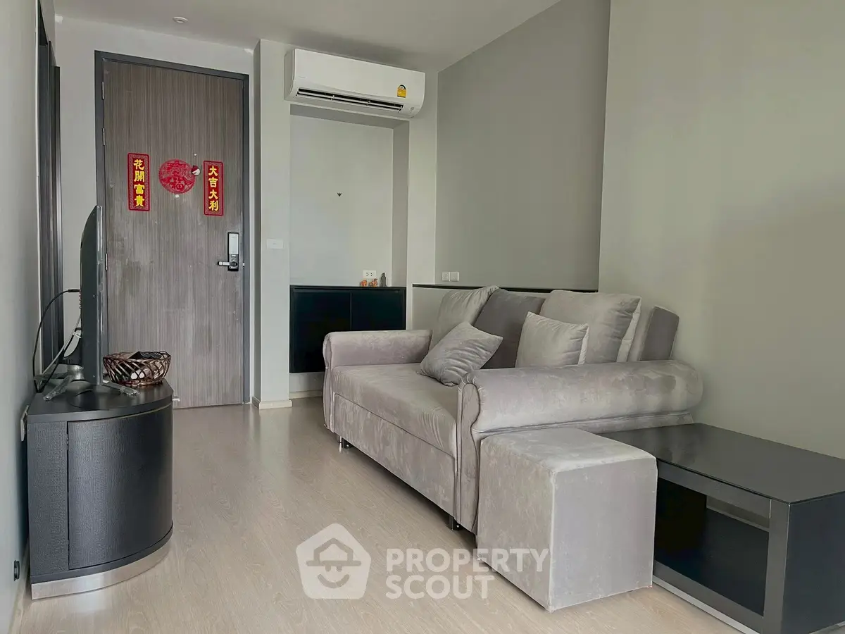 Modern living room with sleek sofa and TV, featuring minimalist decor and air conditioning.