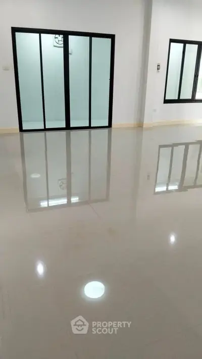 Spacious empty room with glossy tiled flooring and large glass doors.