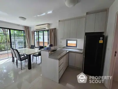 Spacious modern kitchen with dining area and large windows overlooking greenery.