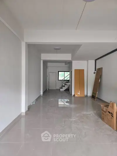 Spacious unfurnished room with glossy tiled floor and staircase view