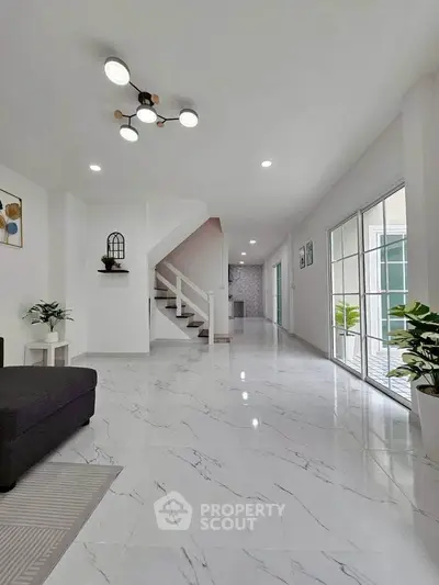 Spacious modern living room with marble flooring and elegant staircase in a bright, airy home.