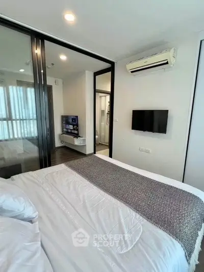 Modern bedroom with air conditioning and TV, featuring sliding glass doors to a living area.