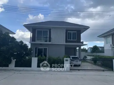 Modern two-story house with driveway and car, surrounded by greenery and clear sky.