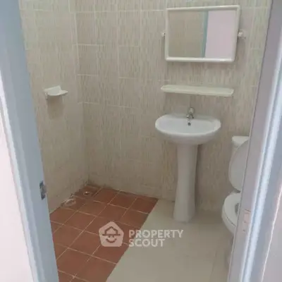 Compact bathroom with pedestal sink and tiled walls, ideal for small spaces.