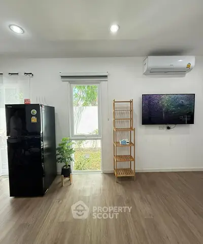 Modern living room with sleek black fridge, wall-mounted TV, and stylish wooden shelving.