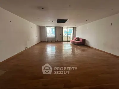 Spacious empty living room with wooden floors and large windows offering city views.