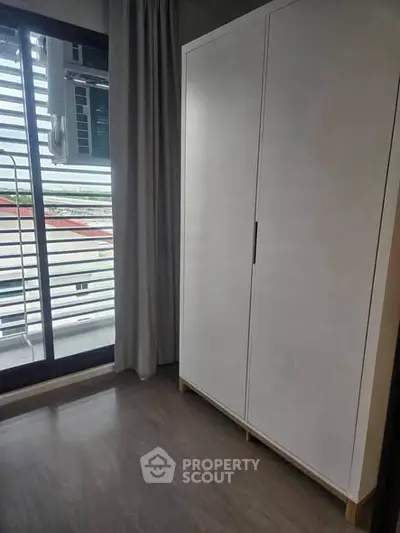 Modern bedroom with sleek wardrobe and large window offering natural light and outdoor view.