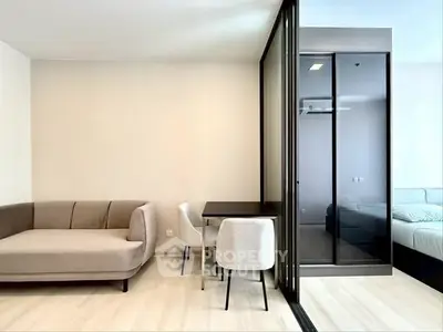 Modern living room with sleek furniture and glass partition leading to bedroom.