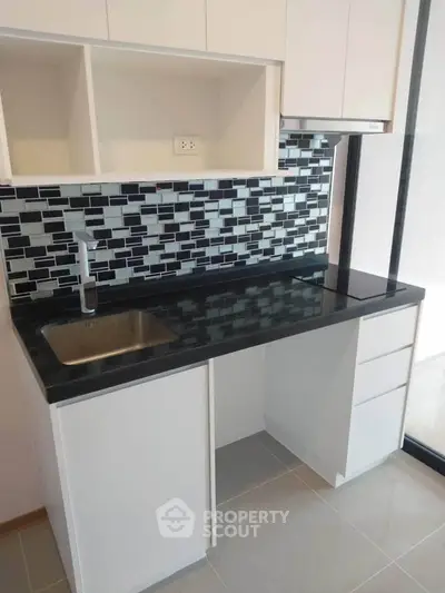 Modern kitchen with sleek black countertop and stylish backsplash in a contemporary apartment.