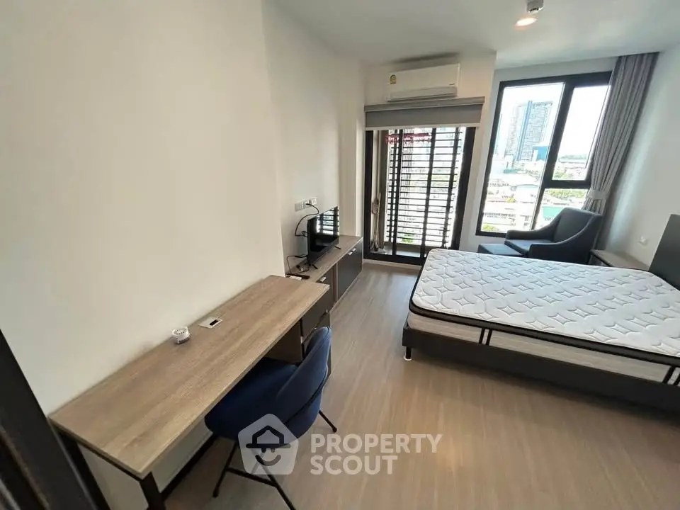 Modern bedroom with city view, featuring a desk, chair, and large window for natural light.