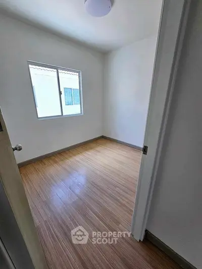 Bright empty bedroom with wooden flooring and large window for natural light.