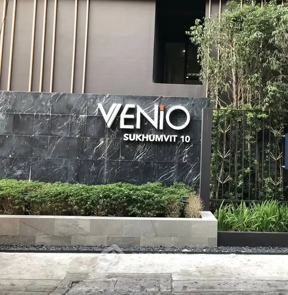 Modern building entrance with sleek design and lush greenery at Venio Sukhumvit 10.