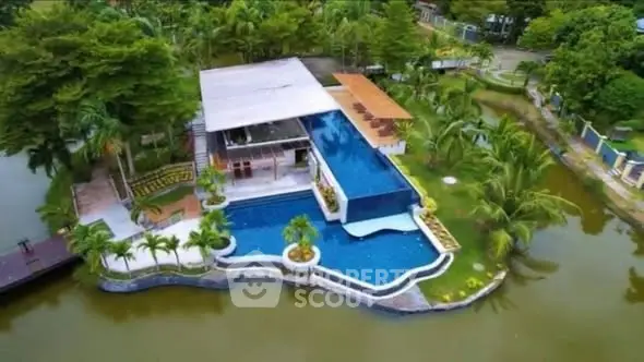 Stunning aerial view of luxury villa with infinity pool surrounded by lush greenery and serene water.