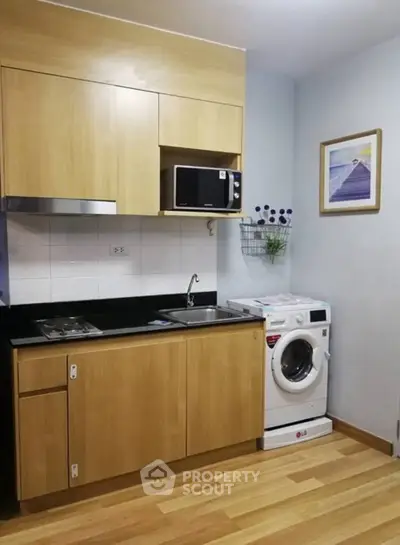 Modern kitchen with wooden cabinets, microwave, and washing machine in compact layout.