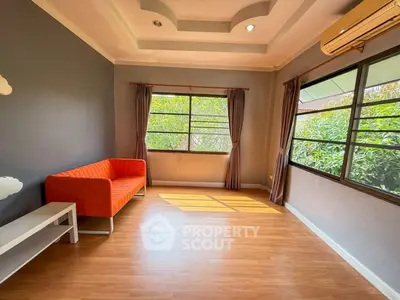 Spacious living room with large windows and vibrant orange sofa, offering abundant natural light and garden views.