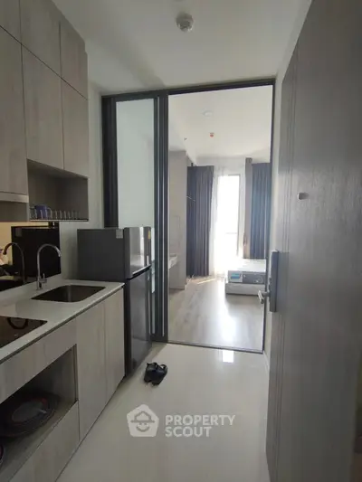 Modern compact kitchen with sleek cabinetry and view into a cozy bedroom in a stylish apartment.