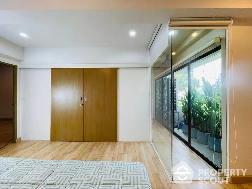 Spacious bedroom with wooden flooring and large glass doors leading to a lush balcony.