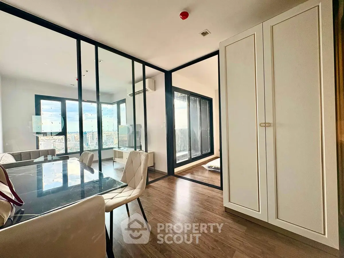 Modern apartment interior with glass partitions and wooden flooring, featuring a dining area and a bright view.