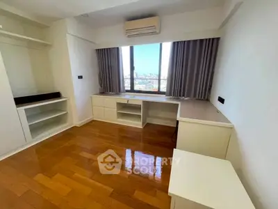 Spacious bedroom with wooden flooring and large window offering city views.