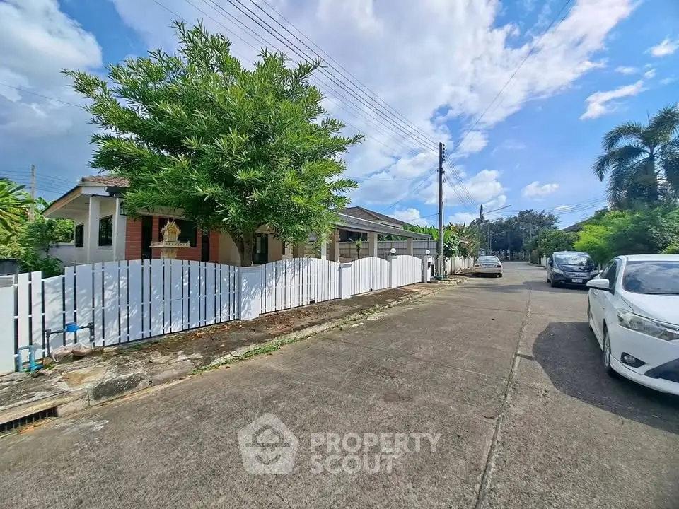 Charming suburban house with white picket fence and lush greenery on a sunny day.