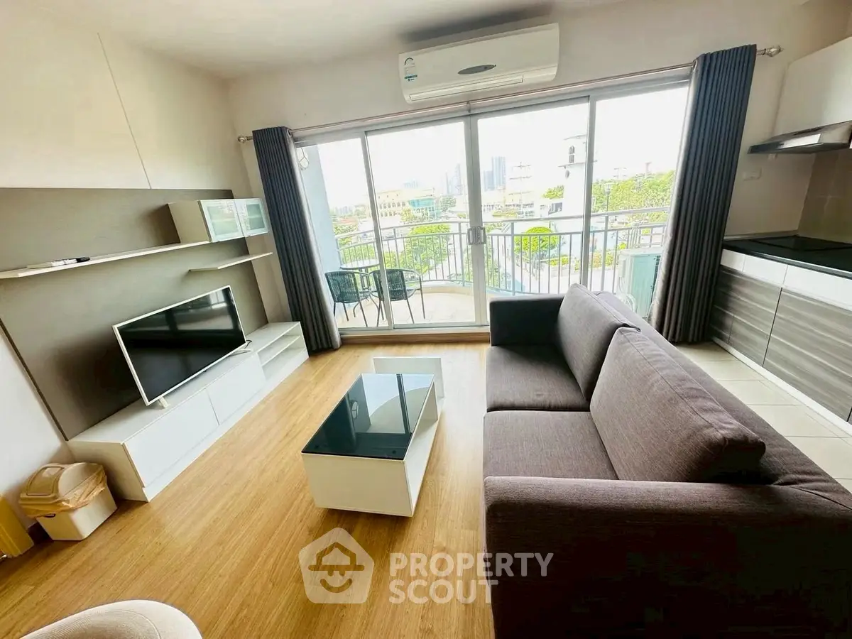 Modern living room with balcony view, sleek furniture, and open kitchen layout.